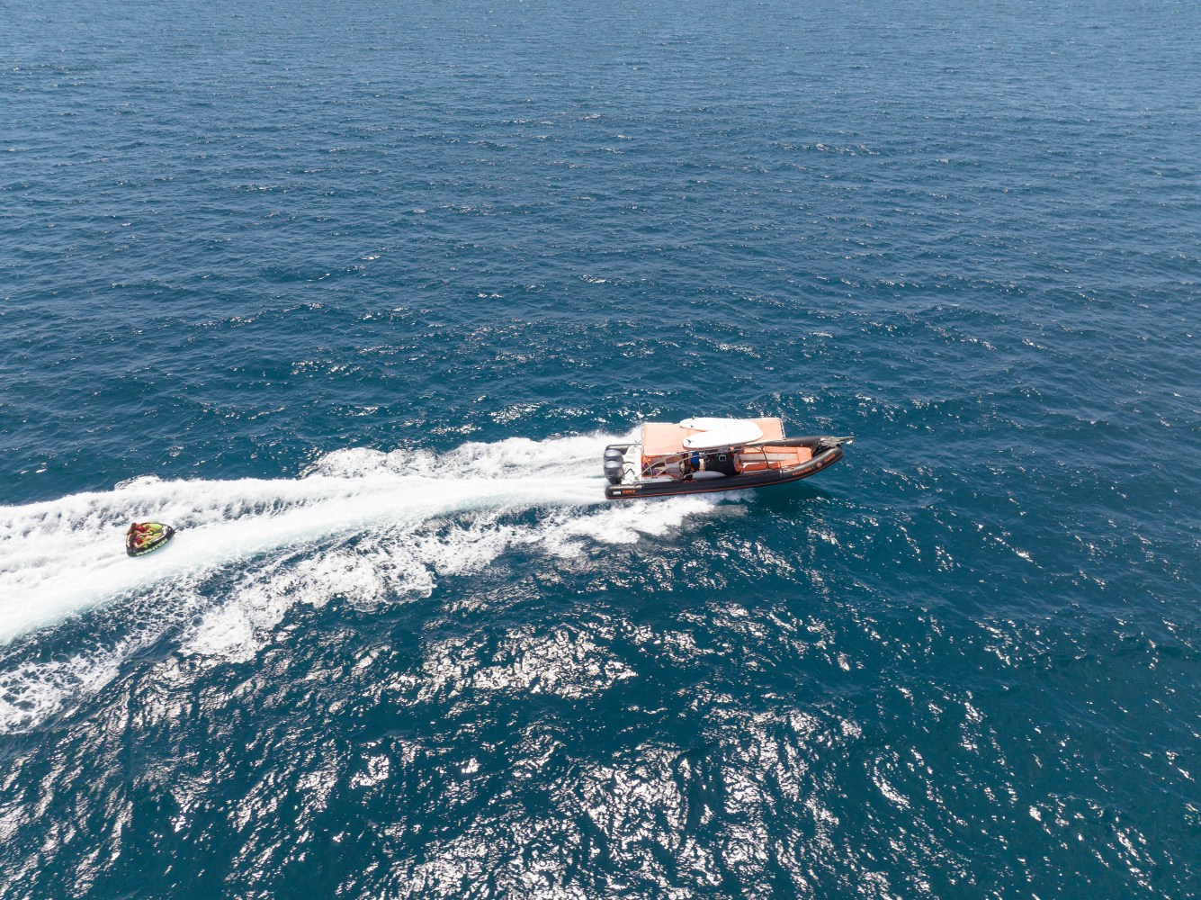 Boat and jet ski moving on open water, leaving white wake trails.
